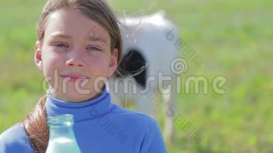 一个男孩在草地上拿着一瓶牛奶的肖像。 一个男孩在田里的奶牛旁边喝牛奶。 健康的生活方式。